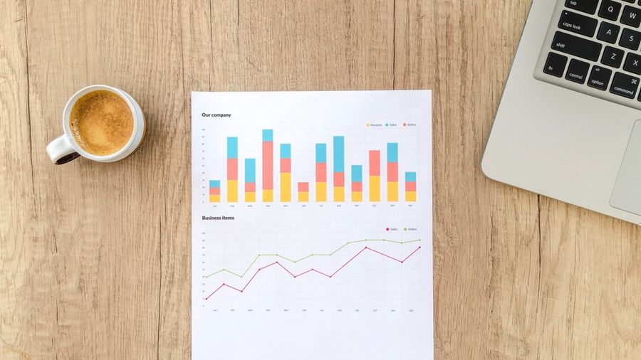 Printed rental cash flow charts beside a laptop and coffee on a wooden desk